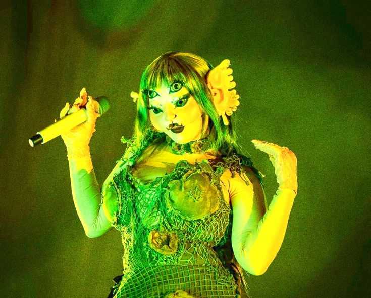 a woman dressed in green holding a microphone and looking at the camera while performing on stage