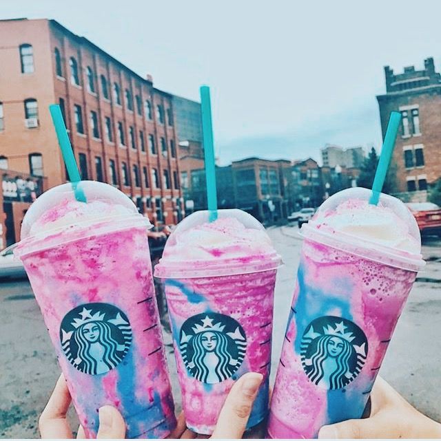 two starbucks drinks with pink and blue swirls are held up in front of the camera