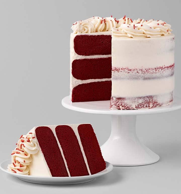 a red velvet layer cake with white frosting on a plate next to the rest of the cake