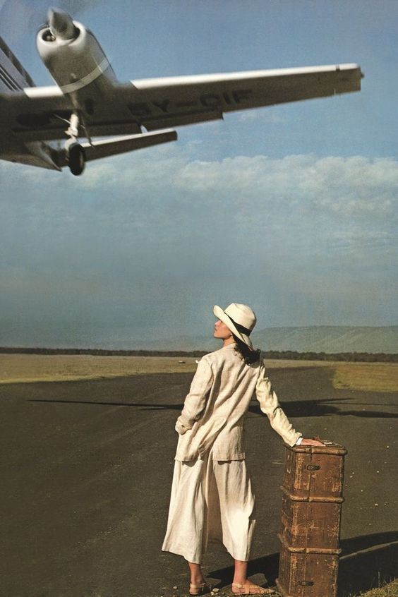 a woman standing next to a suitcase in front of an airplane flying over the ground