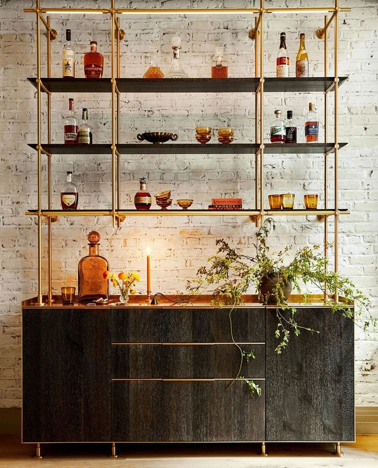 a shelf with bottles and candles on it in front of a brick wall that is filled with shelves