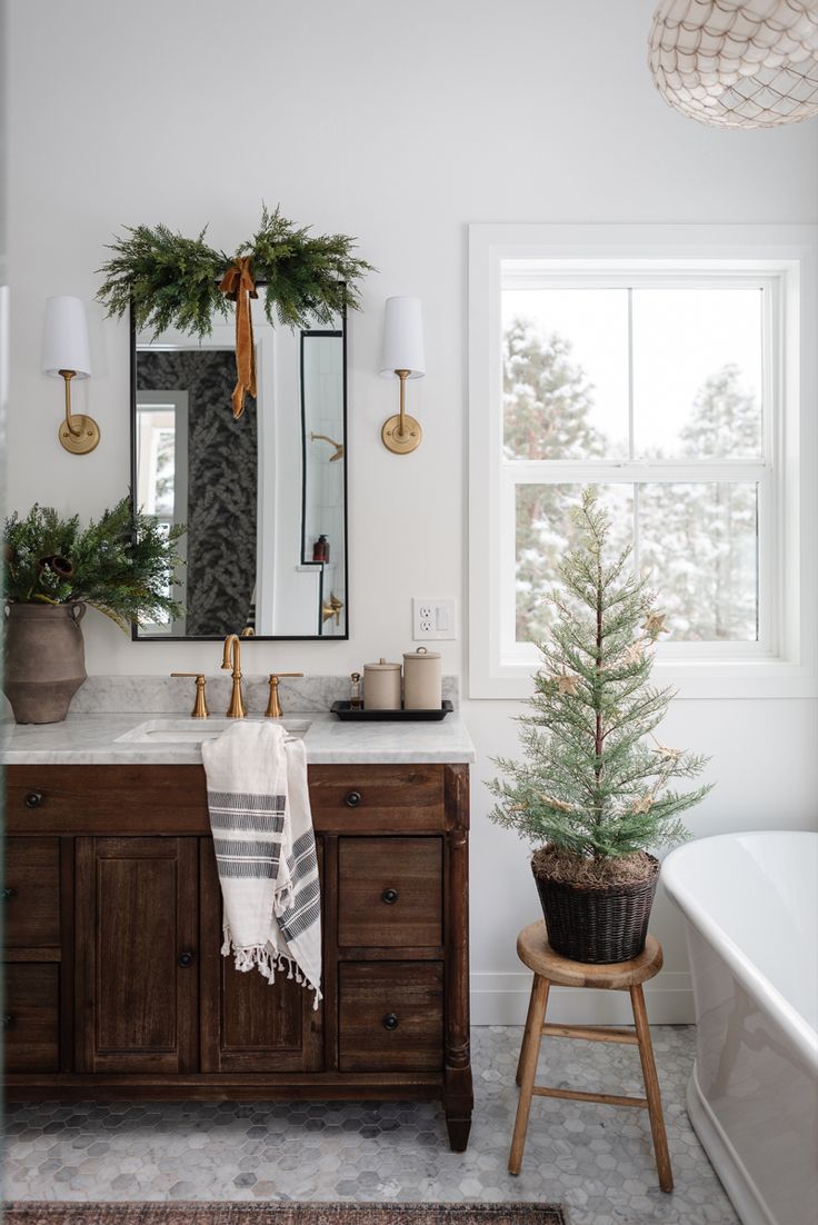 a white bathroom with christmas decorations on the vanity and mirror above it is an evergreen tree