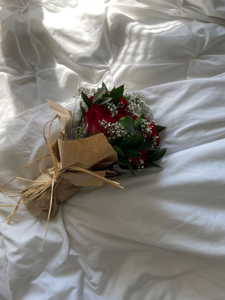 a bouquet of flowers laying on top of a white bed sheet with burlap