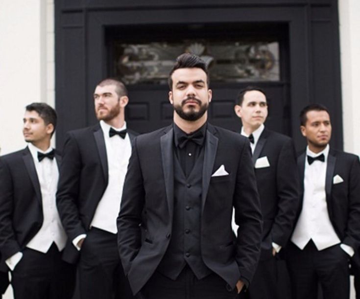 a group of men wearing tuxedos standing in front of a door with their hands in their pockets