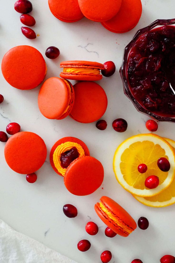 oranges, cranberry sauce and macaroons are arranged on a white surface