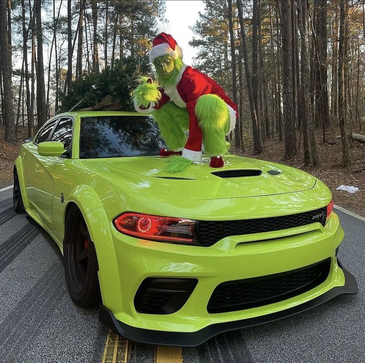 a green car with a santa clause standing on top of it's hood in the road