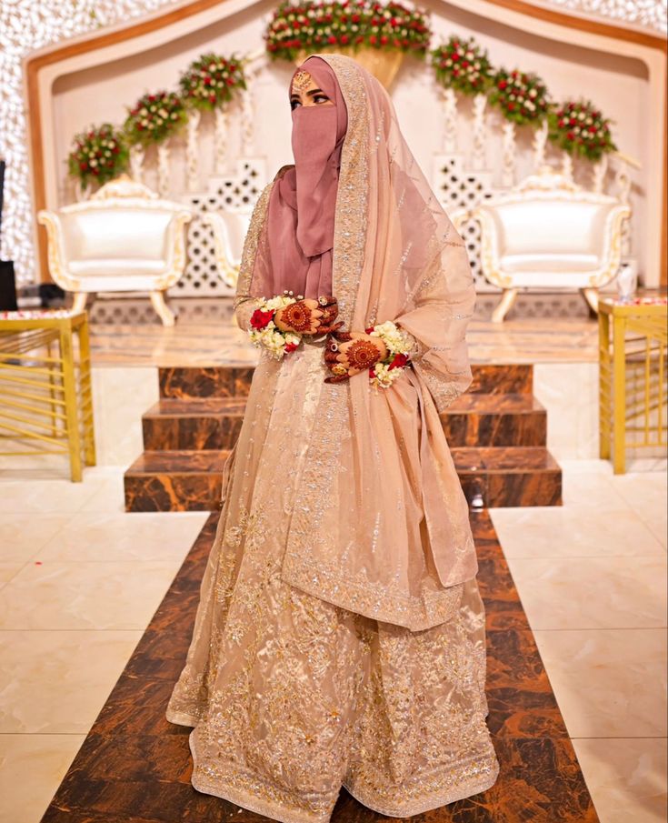 a woman in a hijab stands on a stage with flowers and garlands around her head