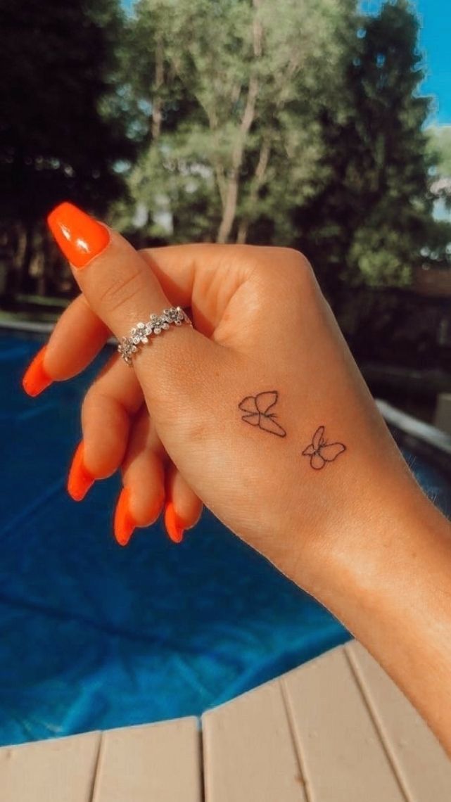 a woman's hand with a small butterfly tattoo on her left wrist, next to a swimming pool