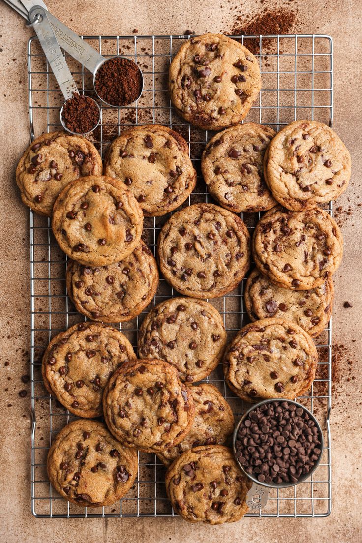 chocolate chip cookies cooling on a wire rack with spoons and cocoa chips next to them