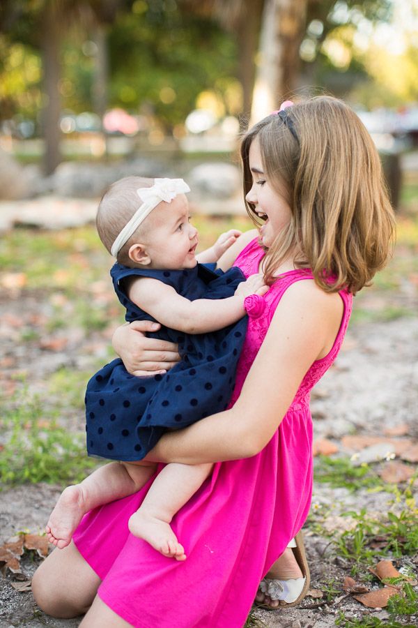 a woman holding a baby in her arms while sitting on the ground with trees in the background