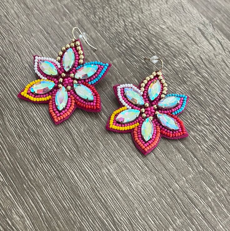 two colorful flower shaped beaded earrings sitting on top of a wooden table