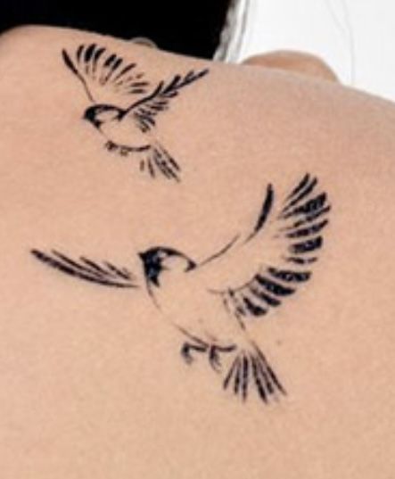 the back of a woman's shoulder with two birds flying around her tattoo design