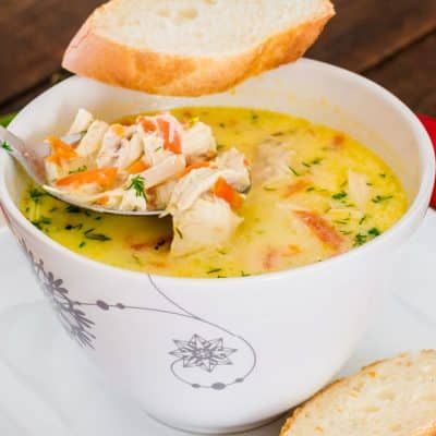 a white bowl filled with chicken soup next to a piece of bread on a plate