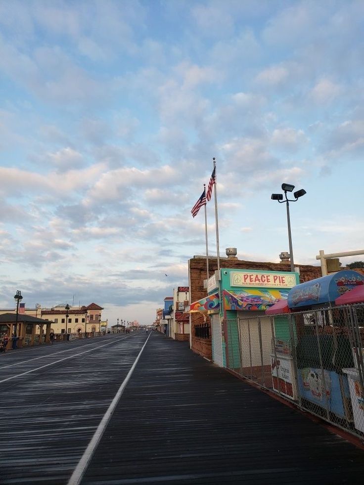 an empty street in the middle of town with shops on both sides and a flag flying high above it