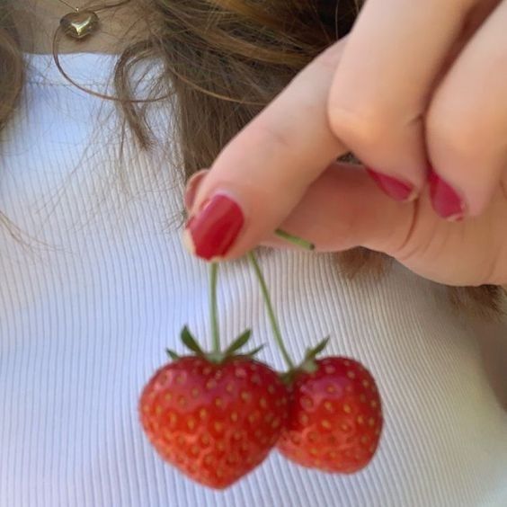 a woman holding two strawberries in front of her face