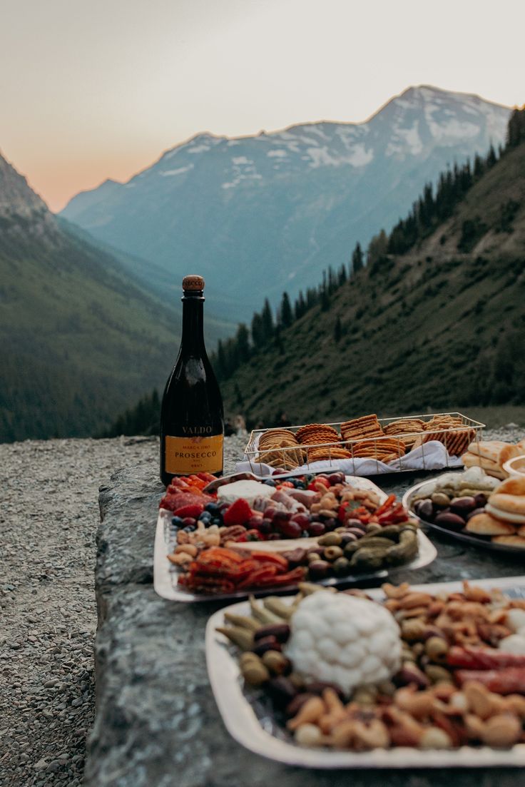 a table full of food and wine with mountains in the background