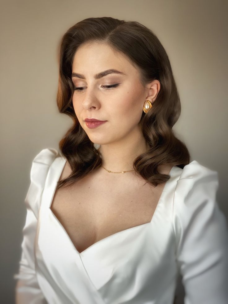 a woman with long hair wearing a white dress and gold earrings is looking down at her left shoulder