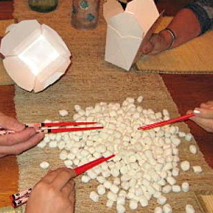 several people sitting at a table with chopsticks and marshmallows