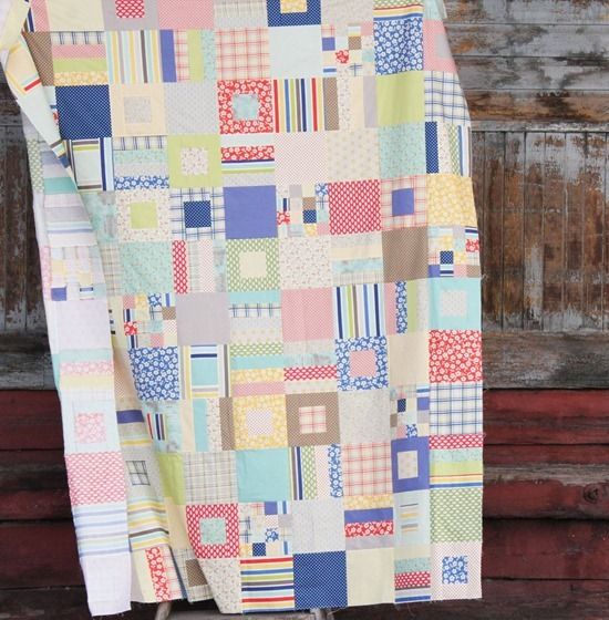 a multicolored patchwork quilt hanging on a clothes rack in front of a wooden wall