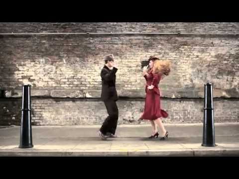 two people are dancing on the sidewalk in front of a brick wall and black poles