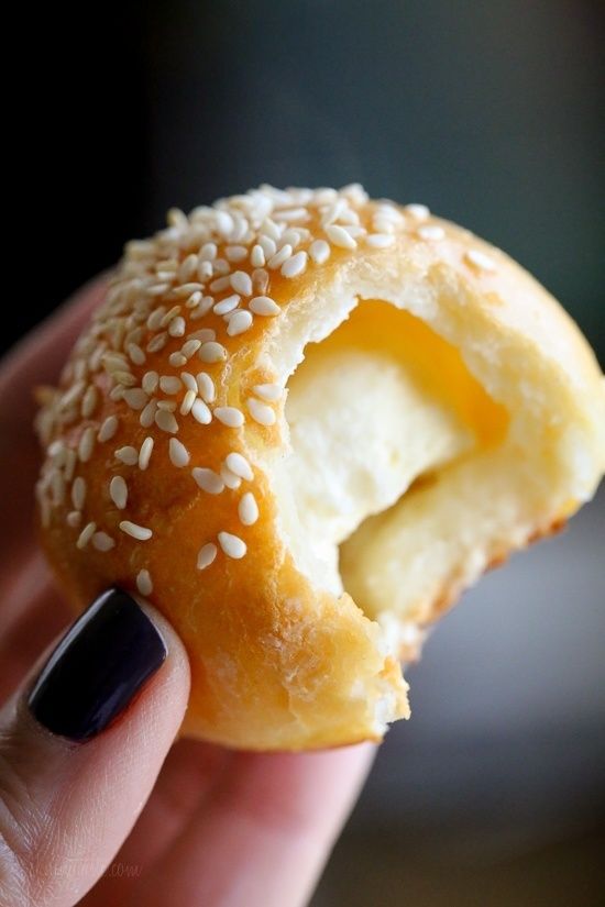 a hand holding a donut with sesame seeds on it and an egg in the middle