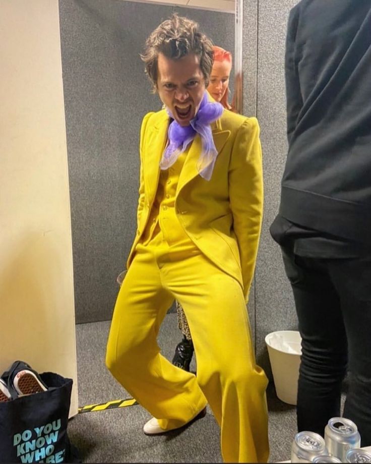 a man in a yellow suit and purple bow tie is sitting on the floor next to some water bottles