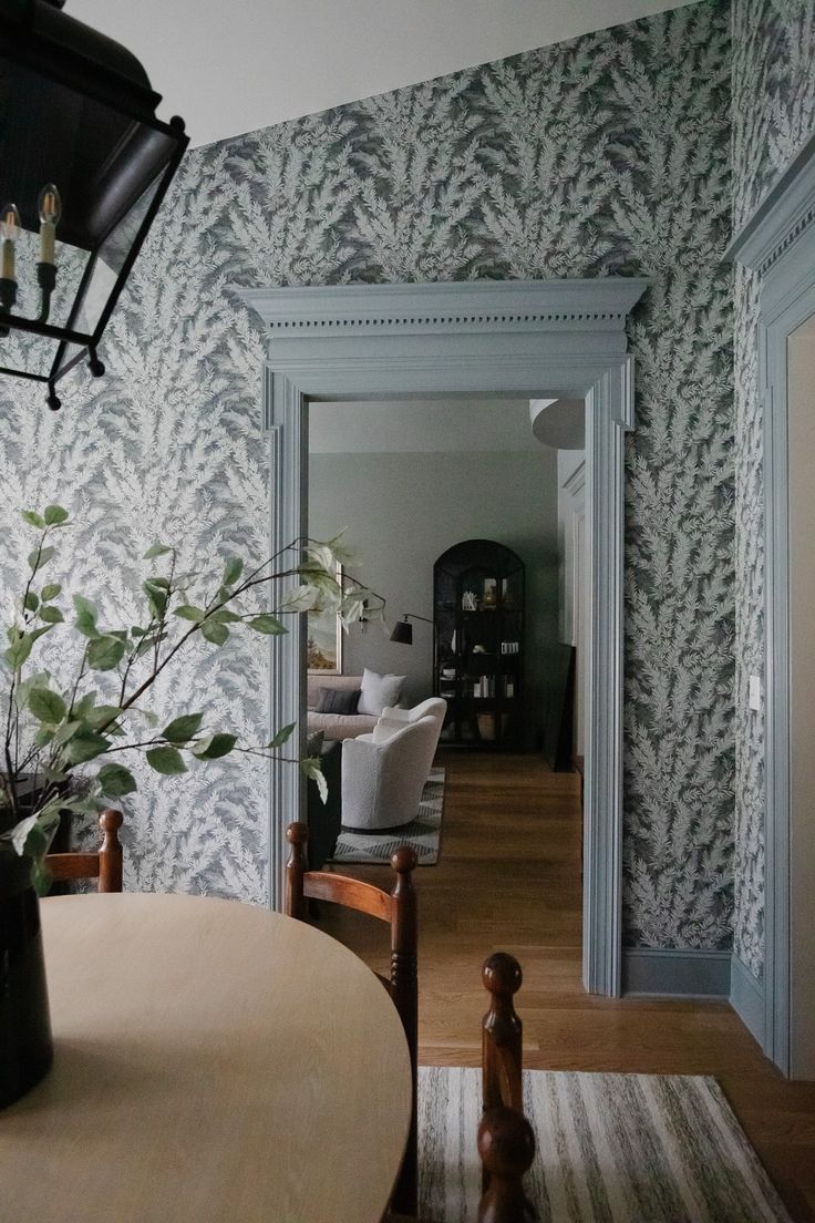 a dining room table with a vase on top of it next to a wallpapered living room