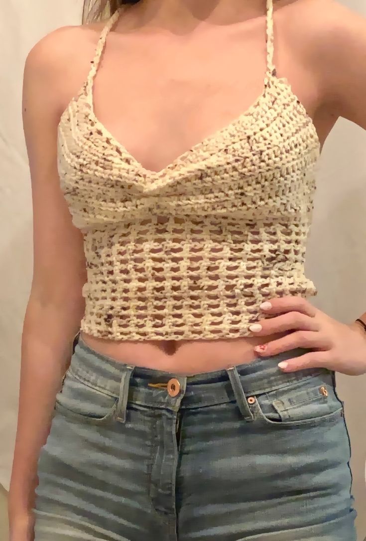 a woman wearing jeans and a crochet top with her hands on her hips