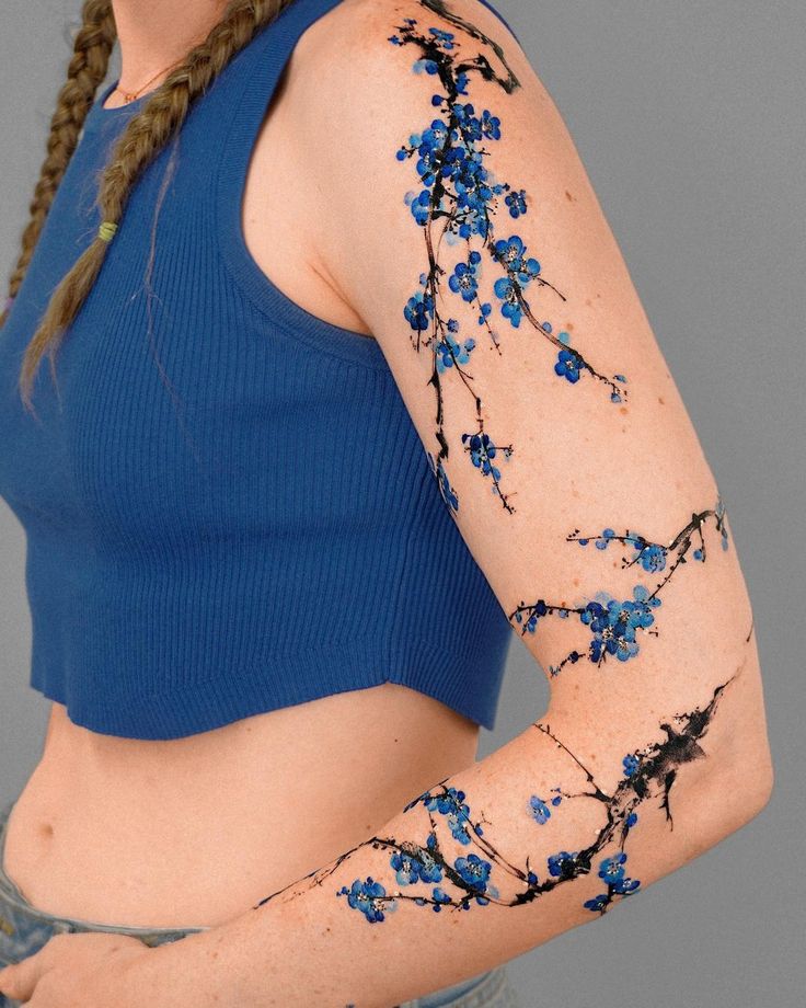 a woman with blue flowers painted on her arm and shoulder, posing for the camera