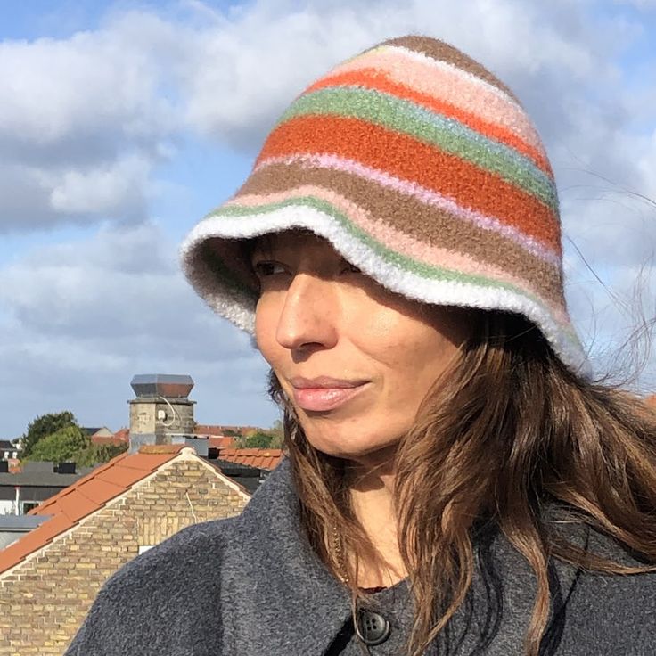 a woman wearing a multicolored knitted hat on top of her head with buildings in the background