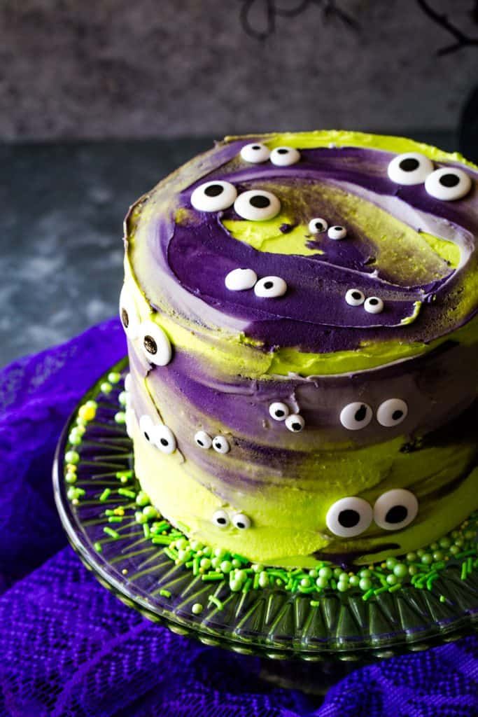 a cake decorated with purple and green frosting has eyes on the icing as decorations