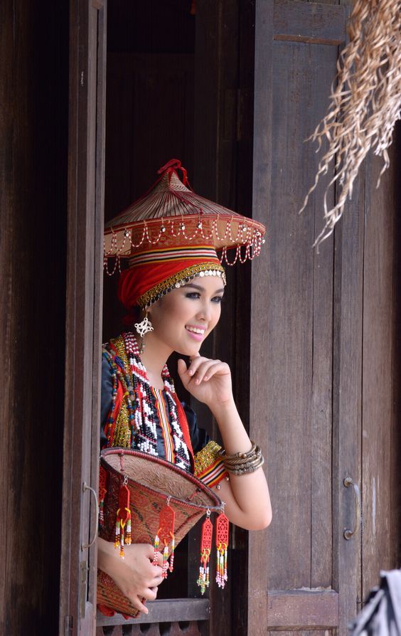 a woman wearing an elaborate headdress and holding a book in her hand while standing next to a wooden door