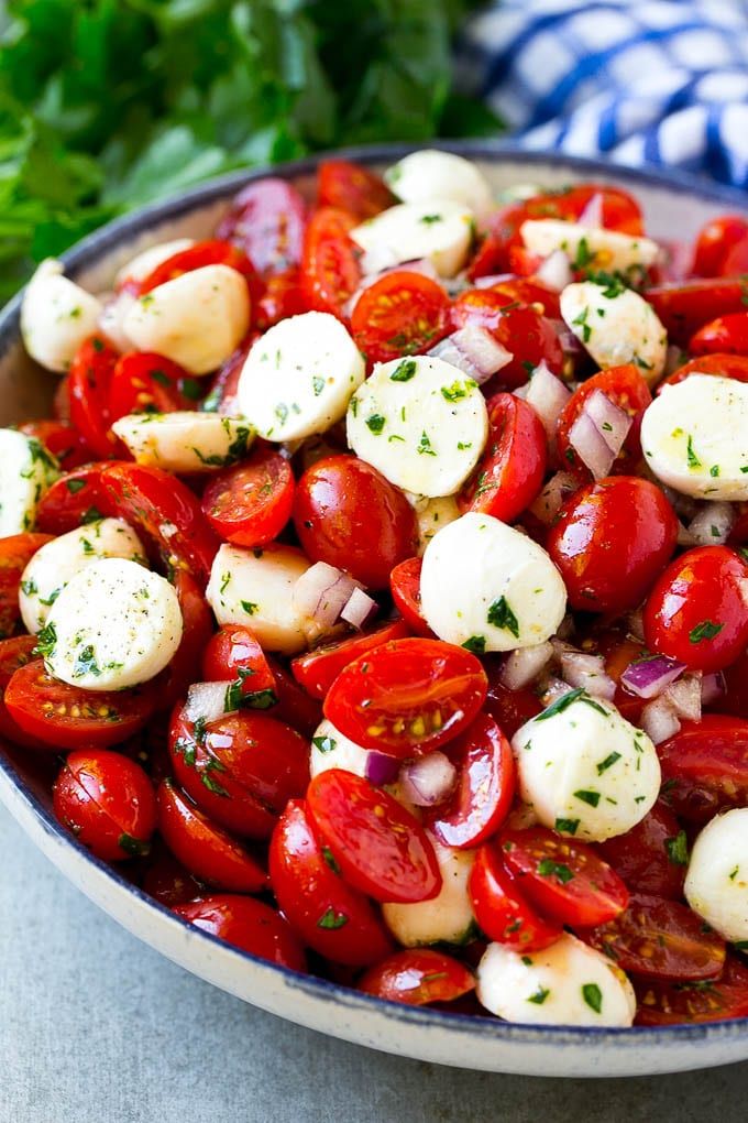 a bowl full of tomatoes and mozzarella with parsley in the back ground