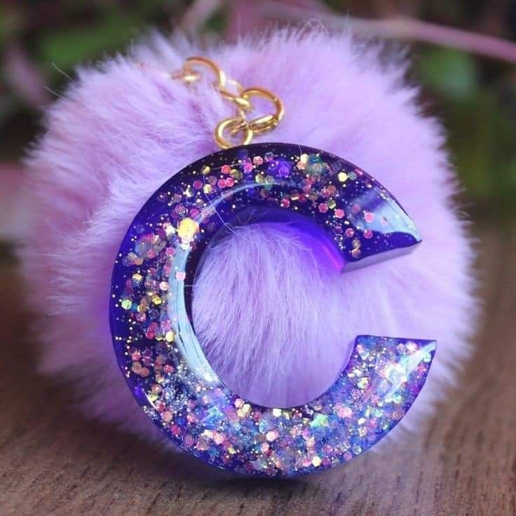 the letter c is made out of glitter and has a furry ball attached to it