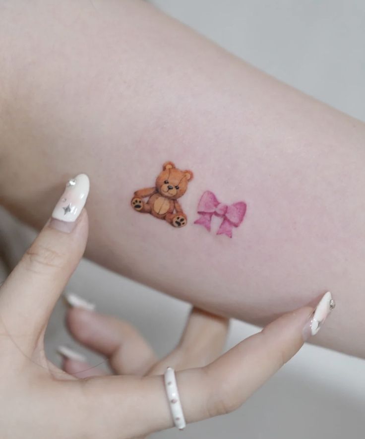 a woman's arm with a small teddy bear tattoo on the left side of her arm