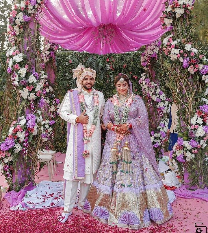 two people dressed in wedding attire standing under an archway with flowers on the ground and petals all around them