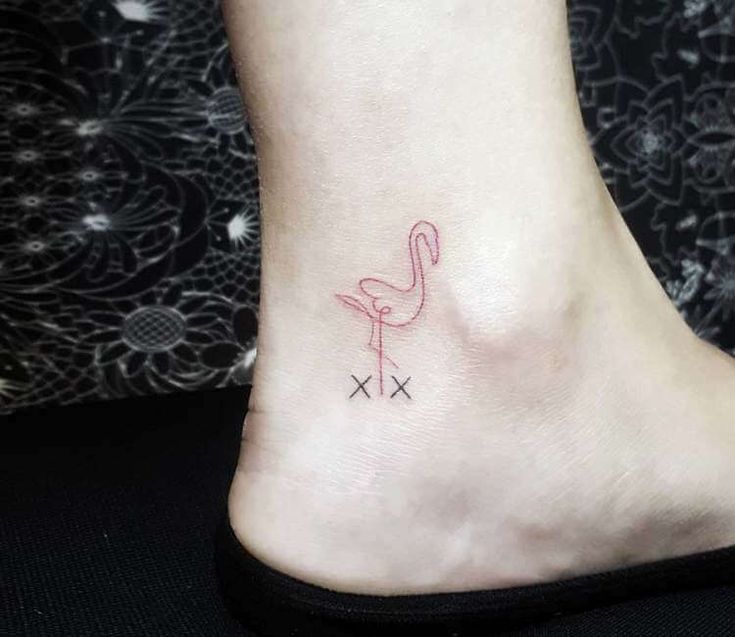 a small pink flamingo tattoo on the side of a foot with crossbones