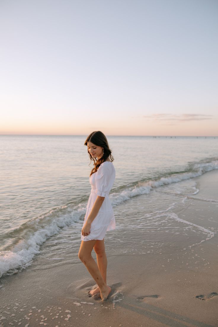 a woman is standing on the beach at sunset