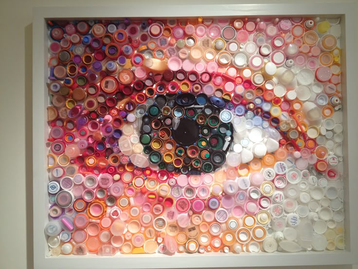 an eye made out of many different colored objects in a white frame on the wall