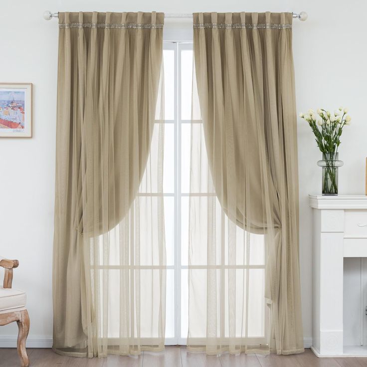 a living room with a white fireplace and large window covered in beige sheer curtain panels