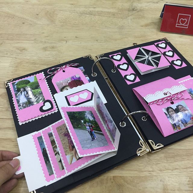 a hand holding an open book with pictures on the pages and pink trimmings