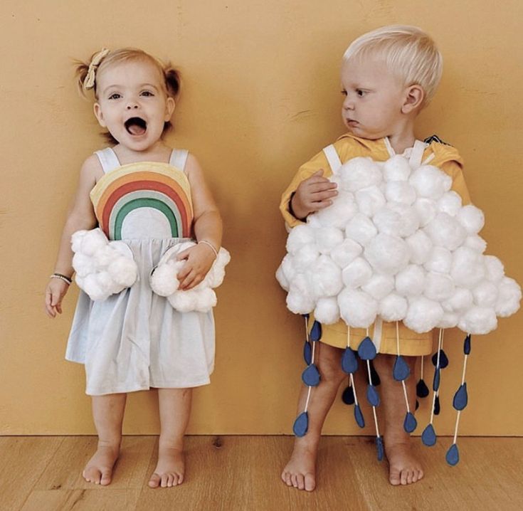 two young children standing next to each other in front of a wall with cotton balls