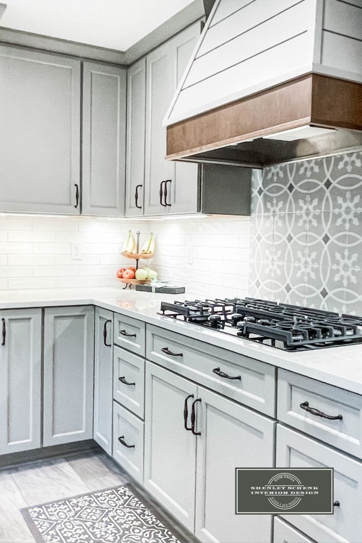 a kitchen with gray cabinets and white counter tops, an oven hood and stove top