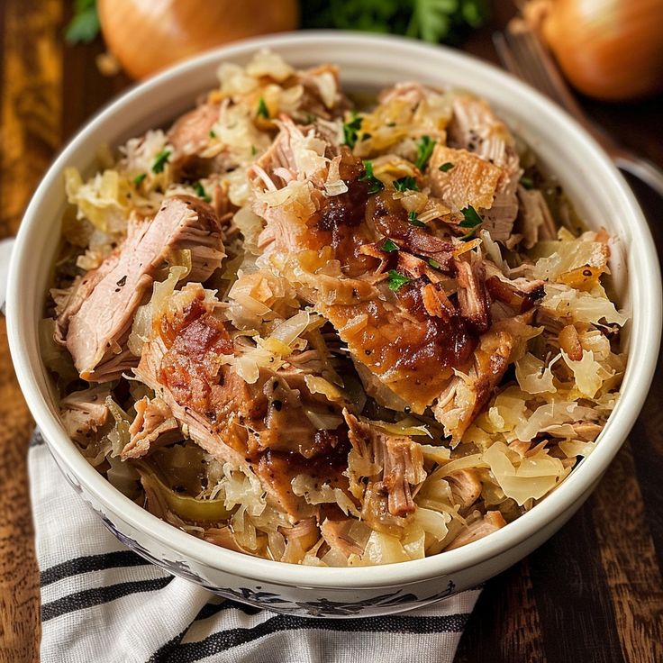 a white bowl filled with meat and vegetables on top of a wooden table next to onions