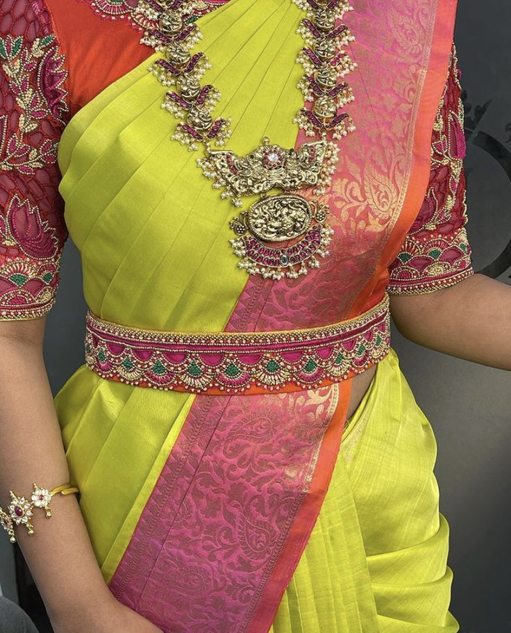 a woman in a yellow and pink sari with gold jewelry on her neckline