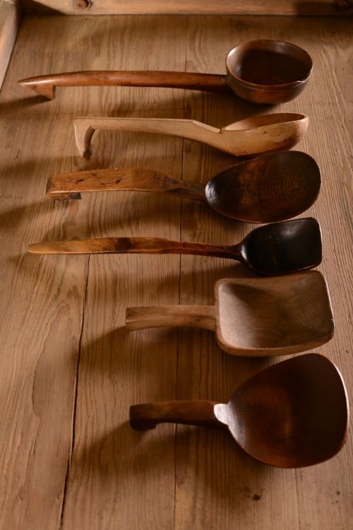 five wooden spoons lined up in a row on top of a wood floor next to a knife