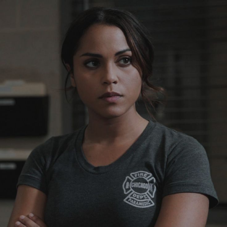 a woman standing with her arms crossed and looking at the camera while wearing a fire department t - shirt