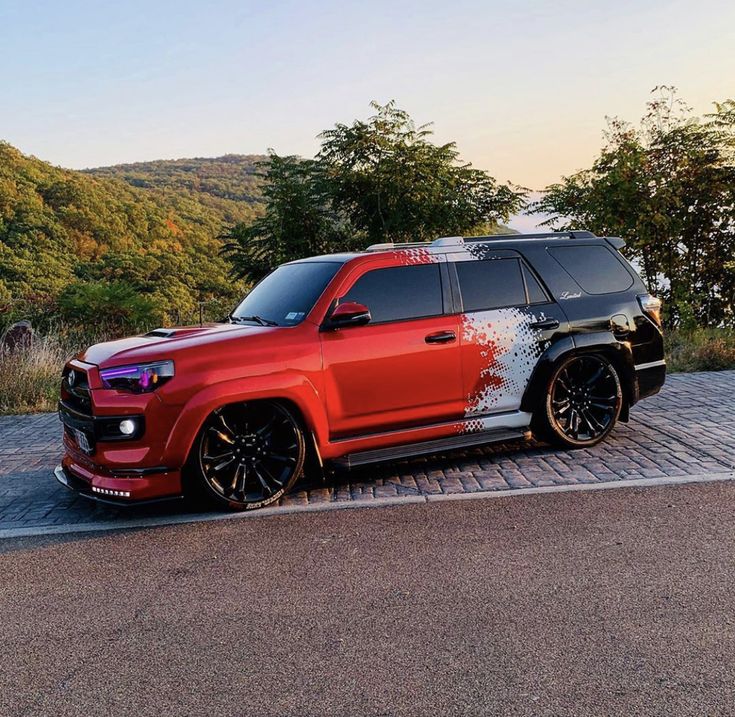 a red suv parked on the side of a road next to some trees and bushes