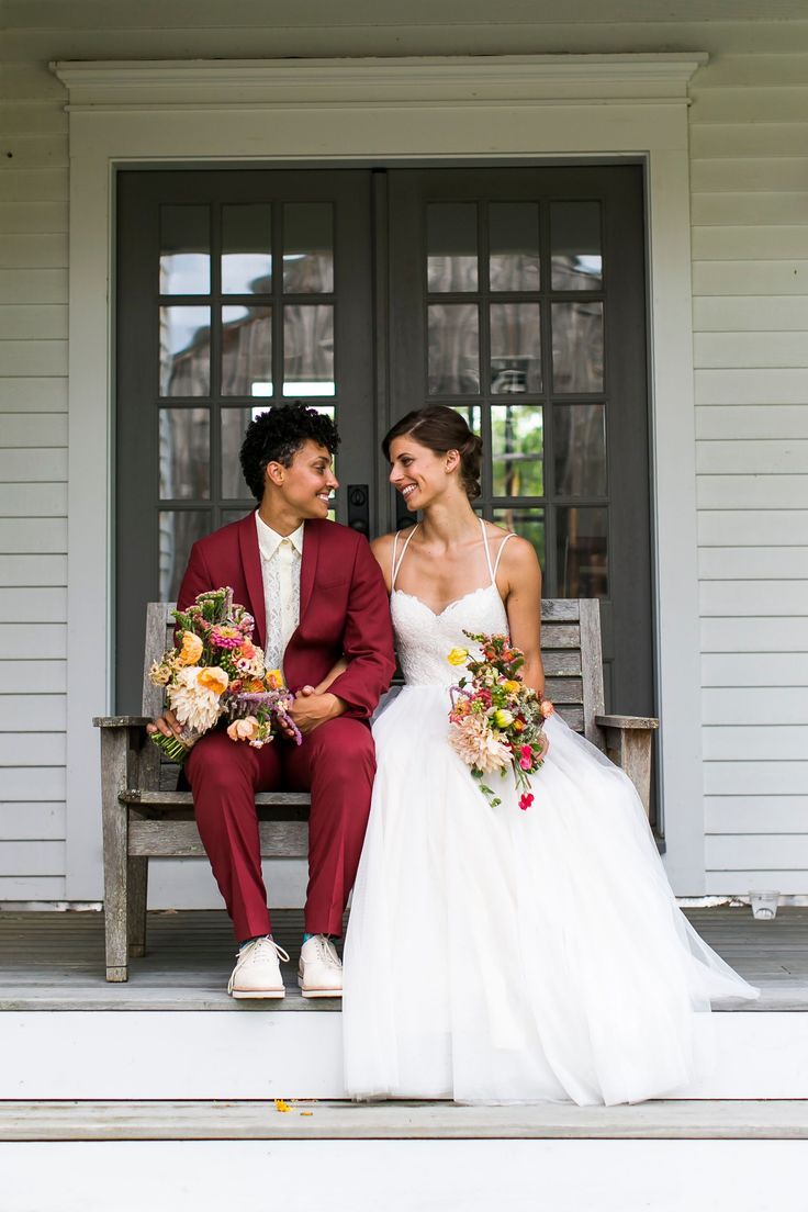 a man and woman sitting on a bench in front of a door holding bouquets