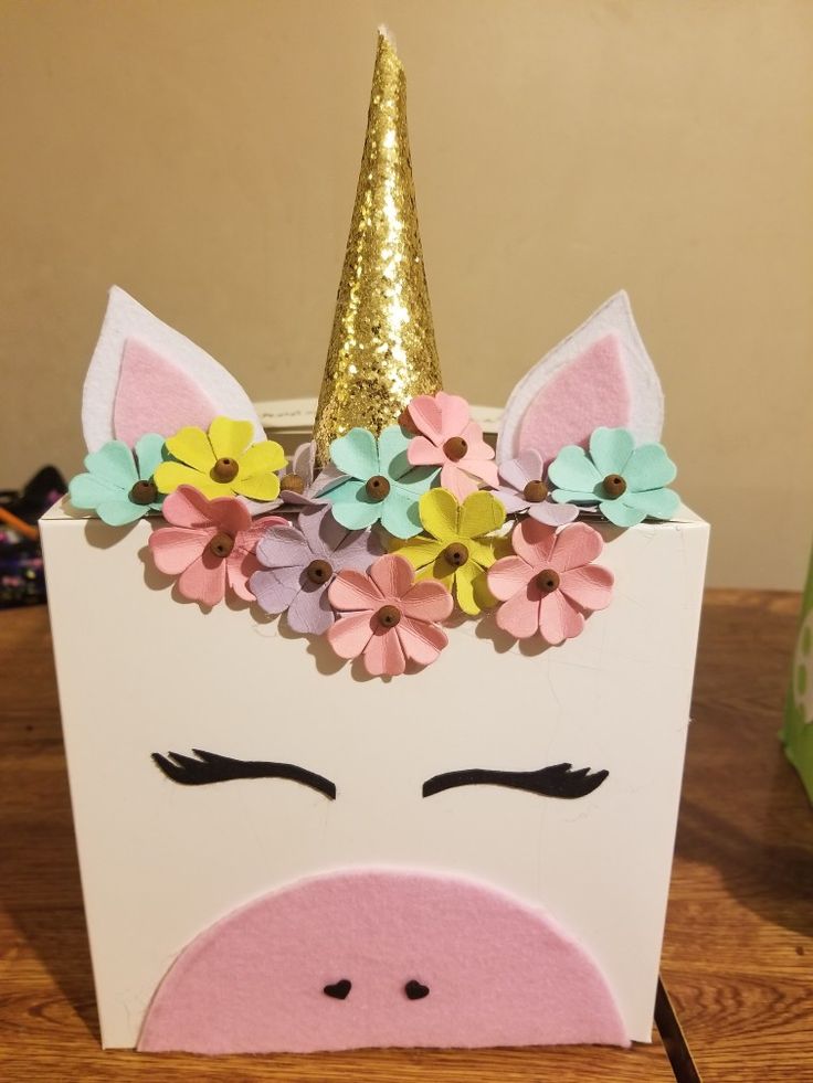 a unicorn head with flowers on it sitting on top of a wooden table next to a green box